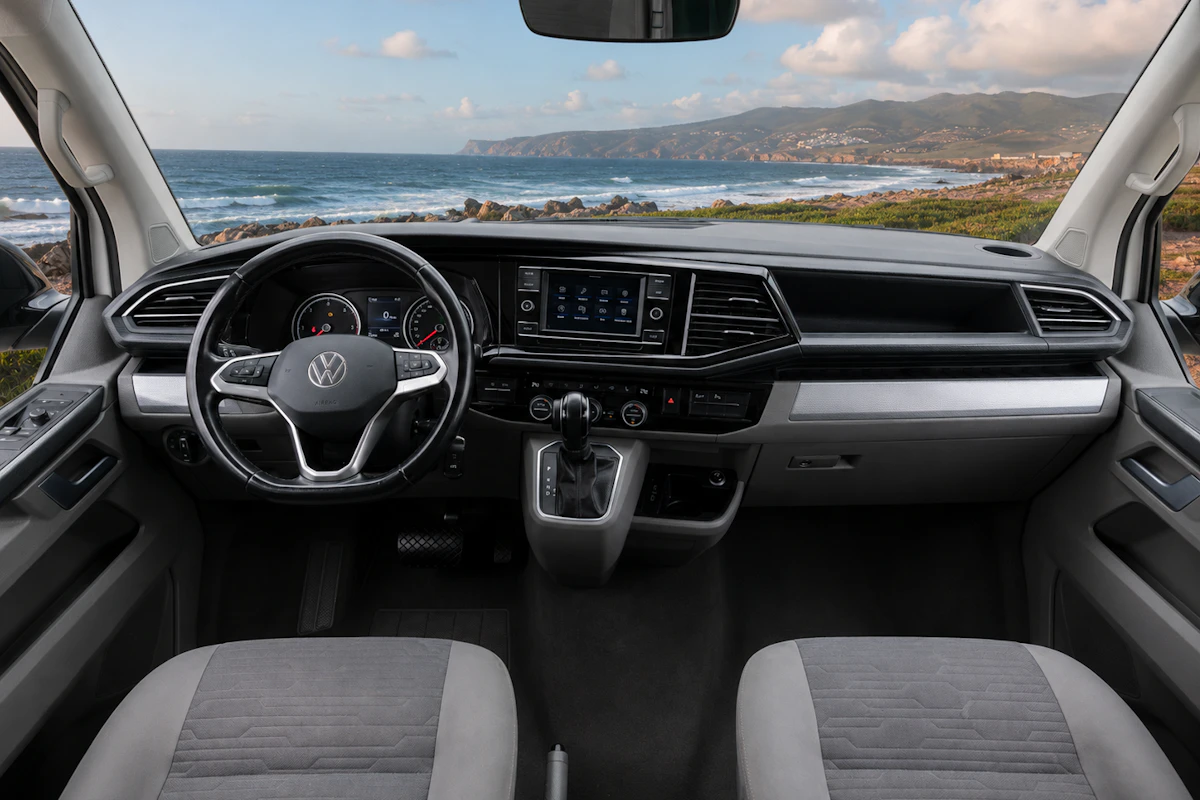 Front cab interior with two seats, steering wheel, dashboard, center console, and infotainment system visible.