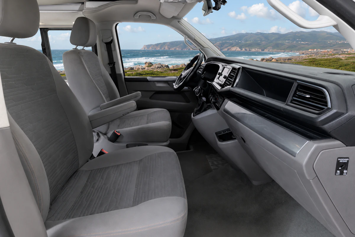 Van interior with two front seats, dashboard, steering wheel, and storage compartments, viewed from the passenger side.