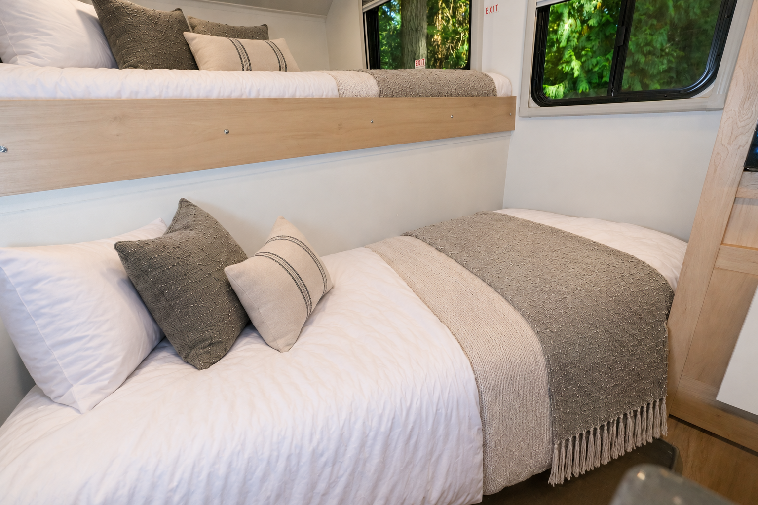 Two bunk beds with pillows and blankets inside a camper van, near a window and wooden panel.