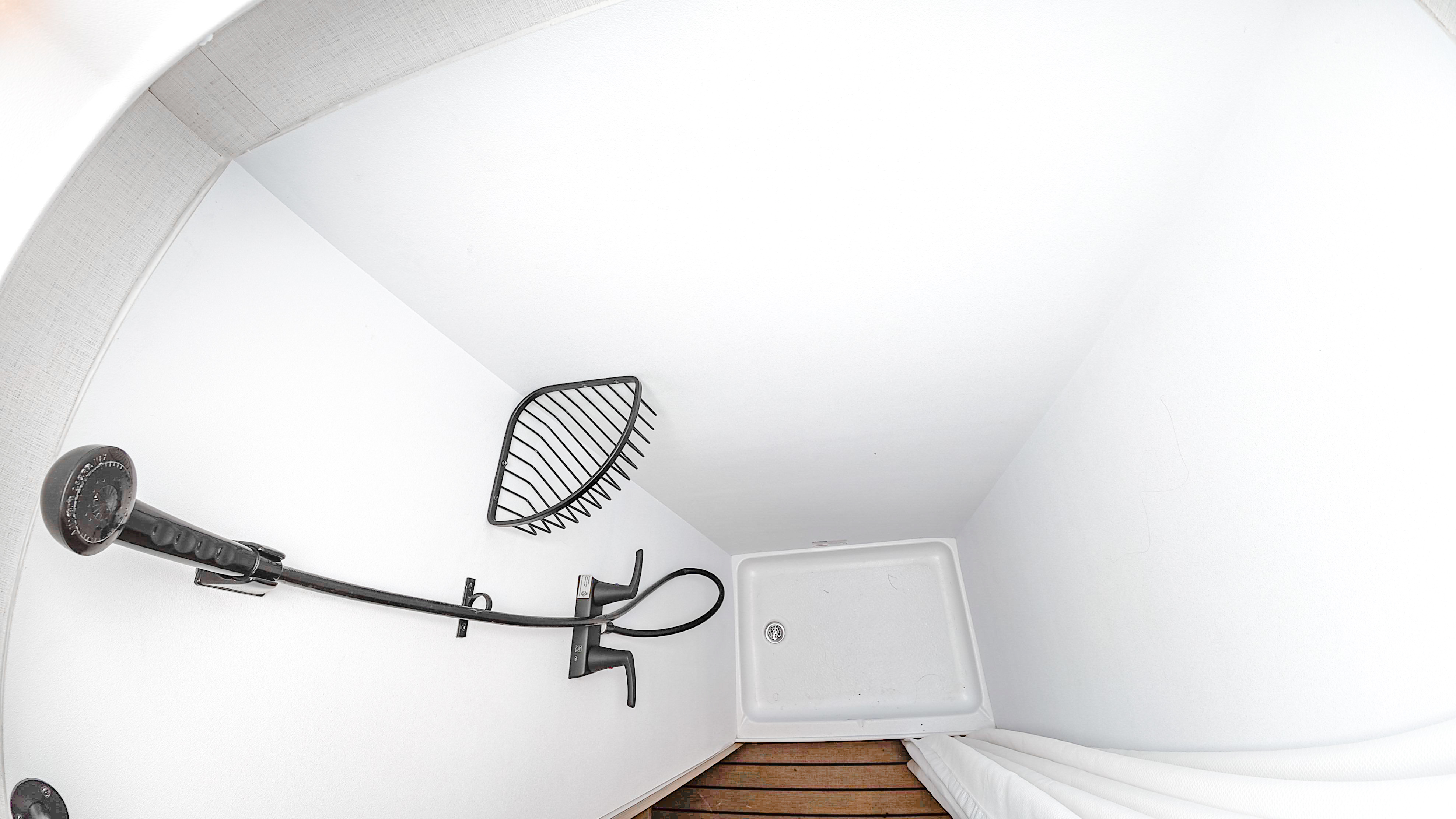 Compact van shower with a wall-mounted showerhead, corner shelf, shower tray, and wooden floor section.