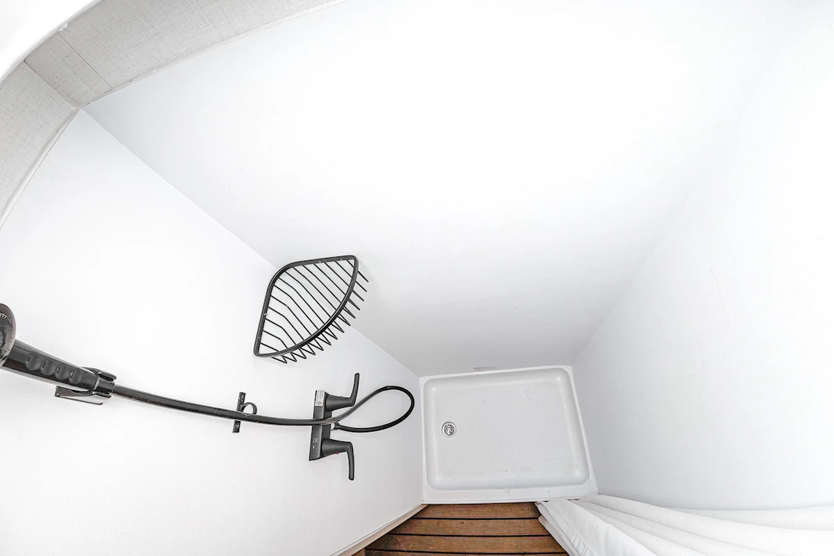 Compact van shower with a wall-mounted showerhead, corner shelf, shower tray, and wooden floor section.