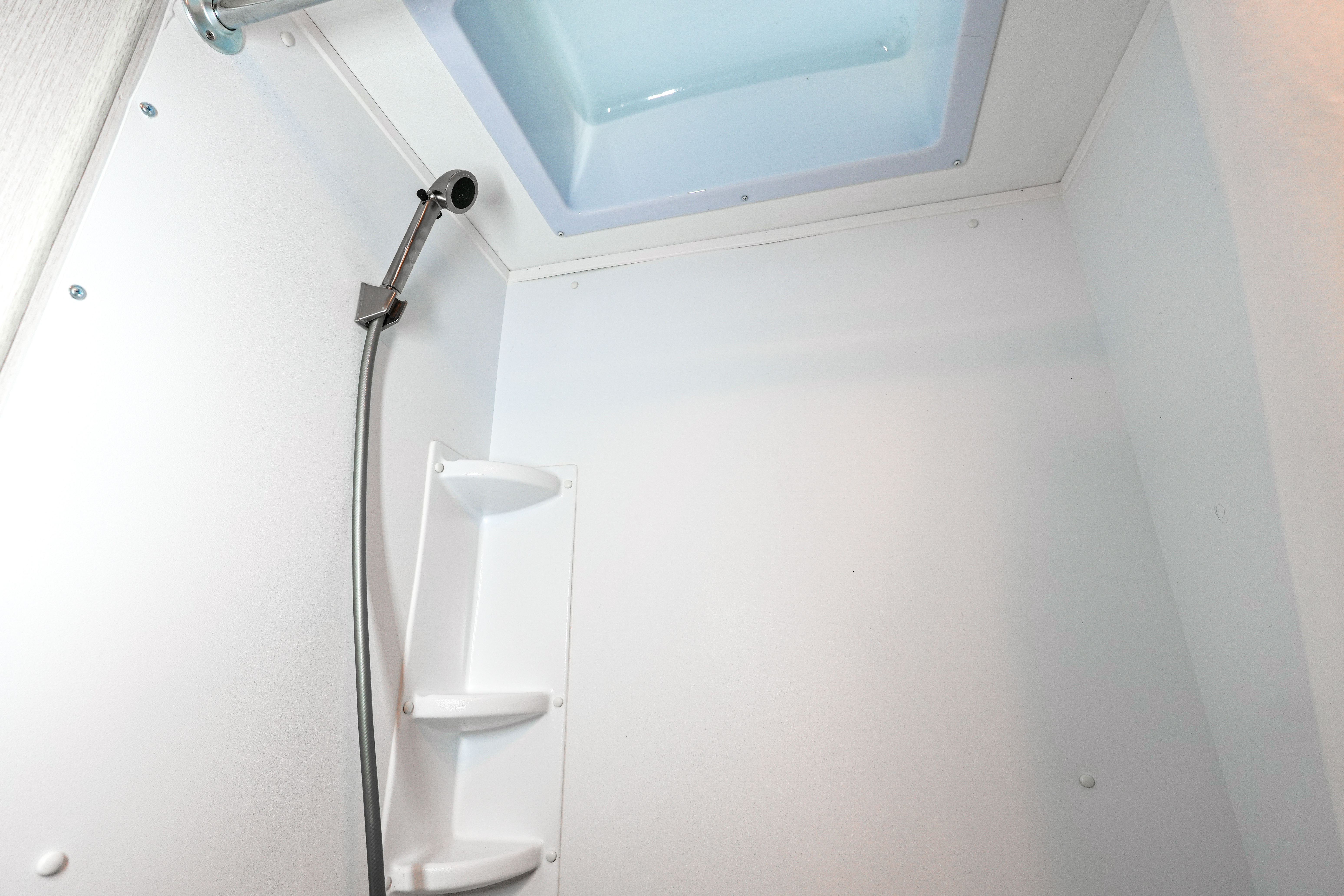 Van interior shower with handheld showerhead, two corner shelves, and a ceiling skylight visible.