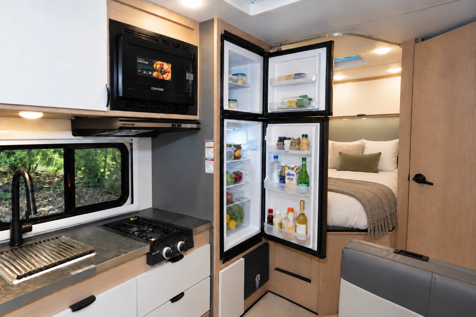 Modern camper van interior with kitchen, open fridge, microwave, sink, stove, and visible rear bed area.