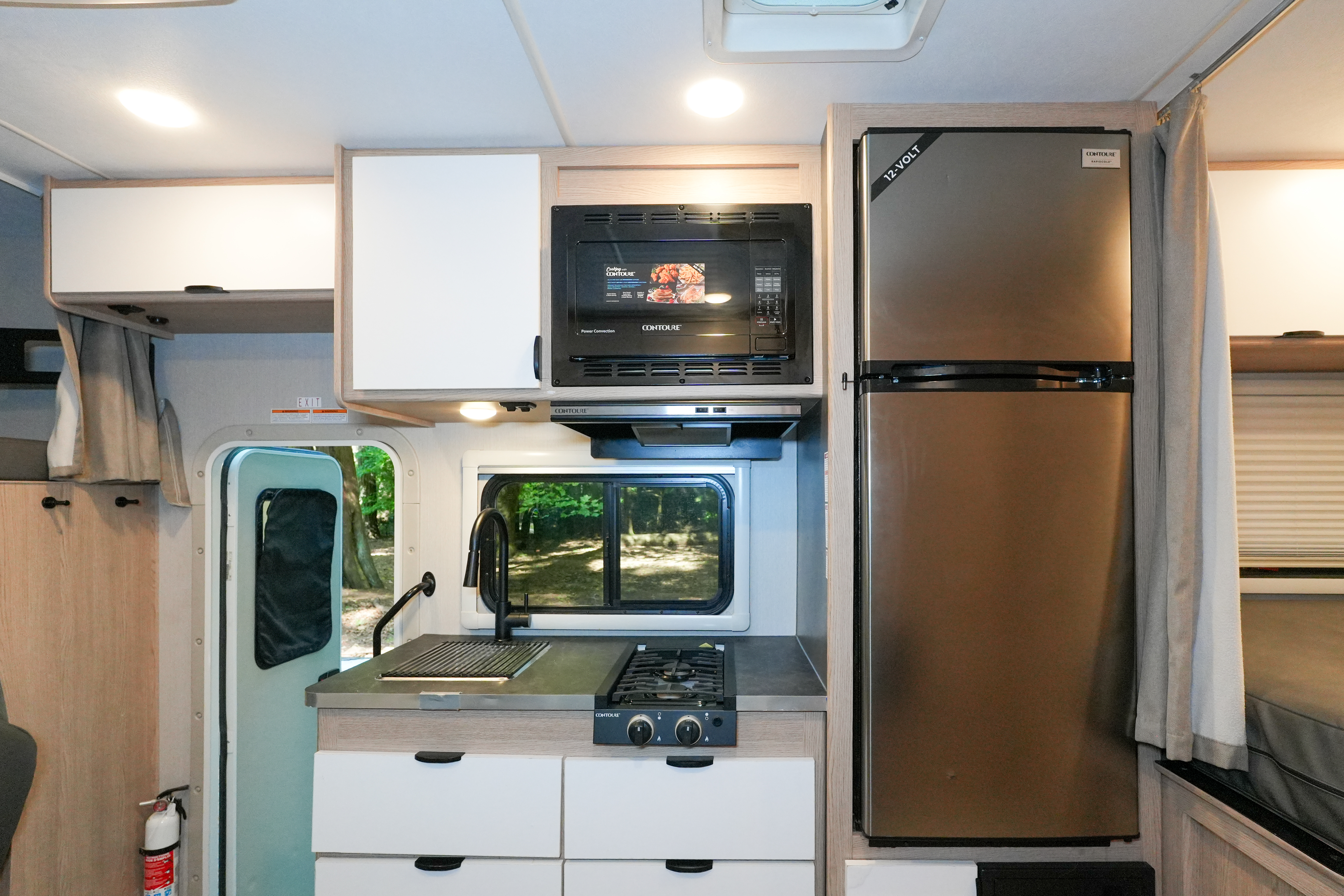 Van interior with kitchen featuring sink, stove, microwave, refrigerator, drawers, and window over the counter.