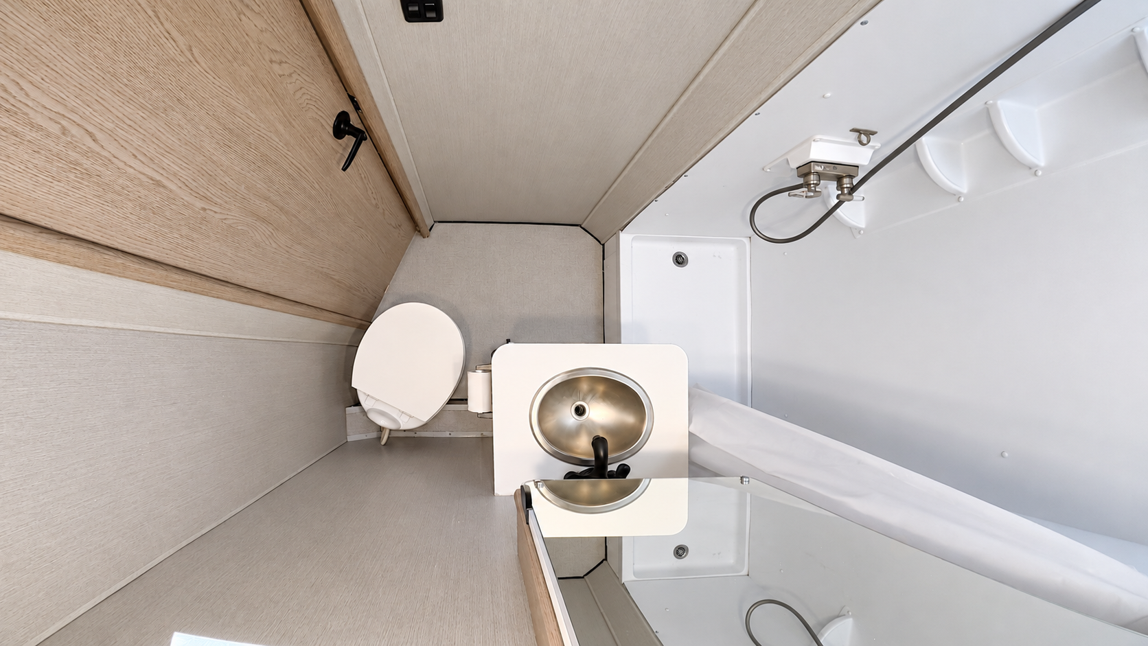 Compact van bathroom with toilet, small sink, mirror, and shower area with handheld showerhead, viewed from above.