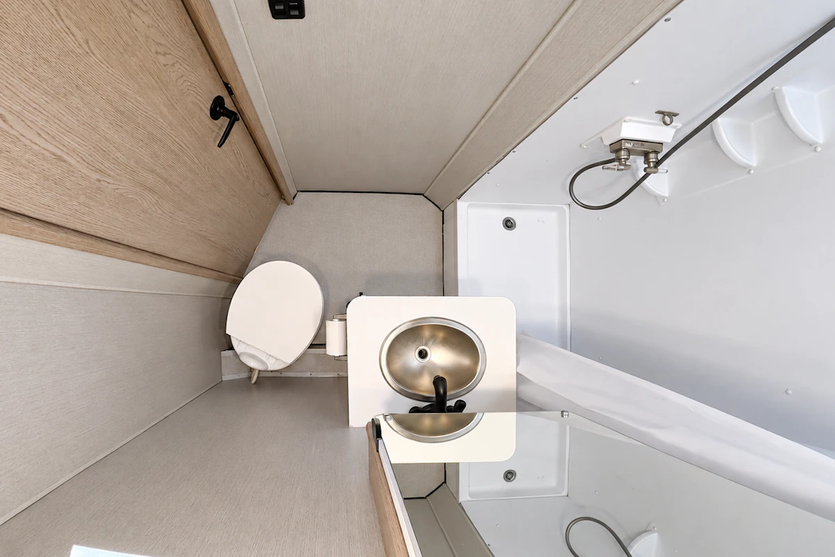 Compact van bathroom with toilet, small sink, mirror, and shower area with handheld showerhead, viewed from above.