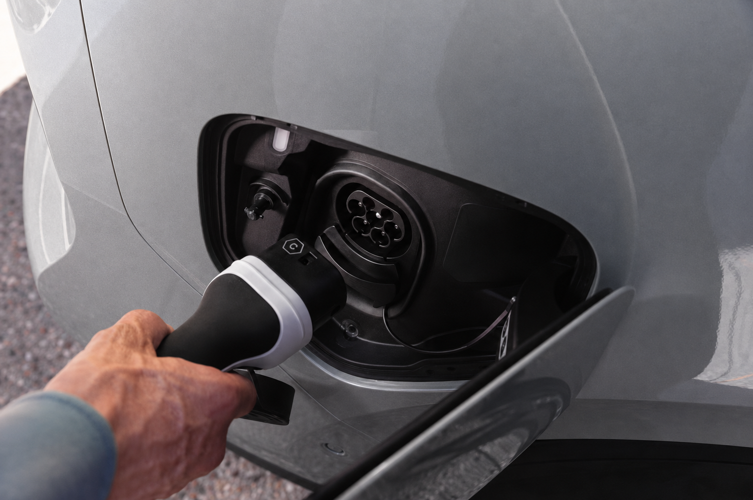 Hand plugging a charging cable into the port of a yellow electric vehicle.