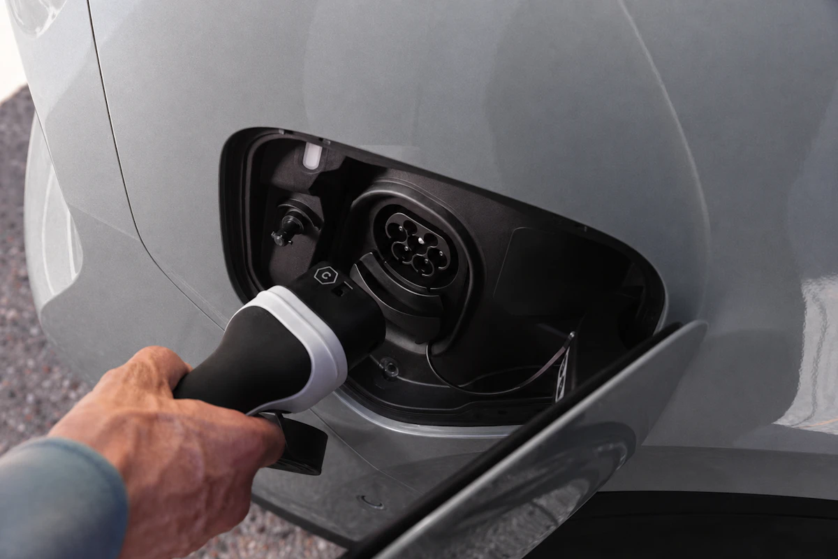 Hand plugging a charging cable into the port of a yellow electric vehicle.
