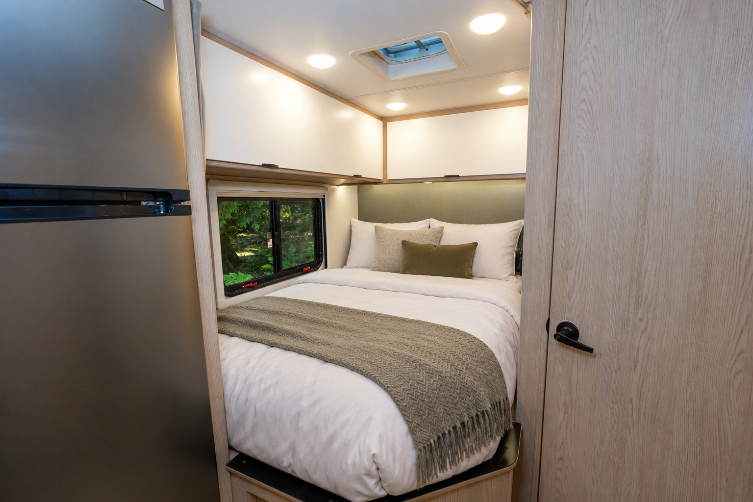 Interior view showing a fixed double bed, overhead cabinets, window, and ceiling vent inside the van.