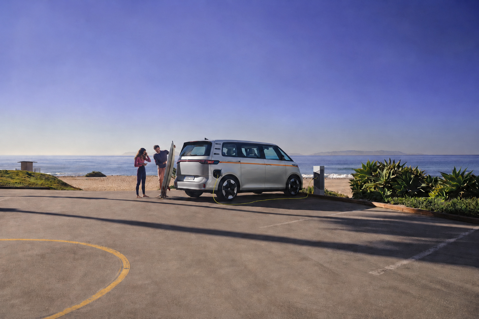 People standing beside a yellow campervan parked near the beach, overlooking the ocean under a clear blue sky.
