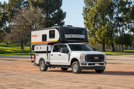 Side view of a large pickup camper van with an over-cab sleeping area and high roof.