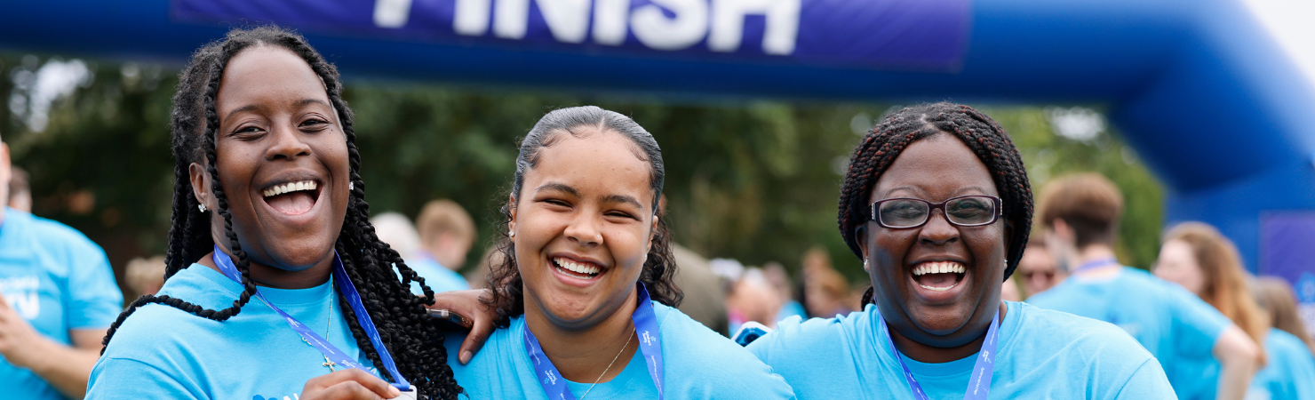 Three ladies wearing #MemoryWalk t-shirts smiling in front of the finish line holding their medals