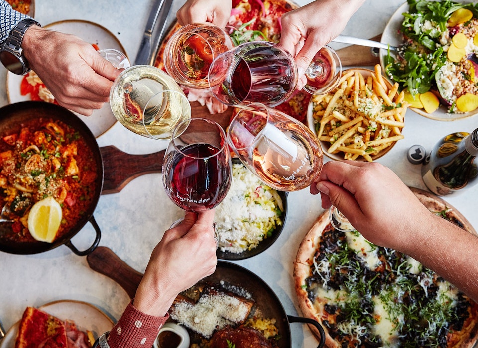 Group of friends clinking wine glasses over table of food