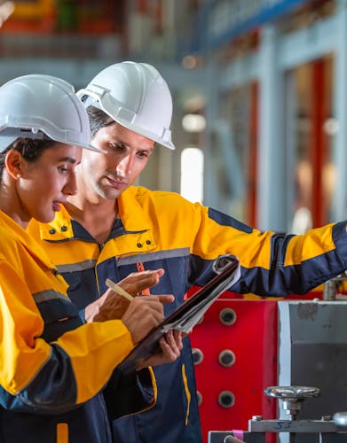 Engineers in hard hats and safety jackets reviewing plans together at an industrial site.
