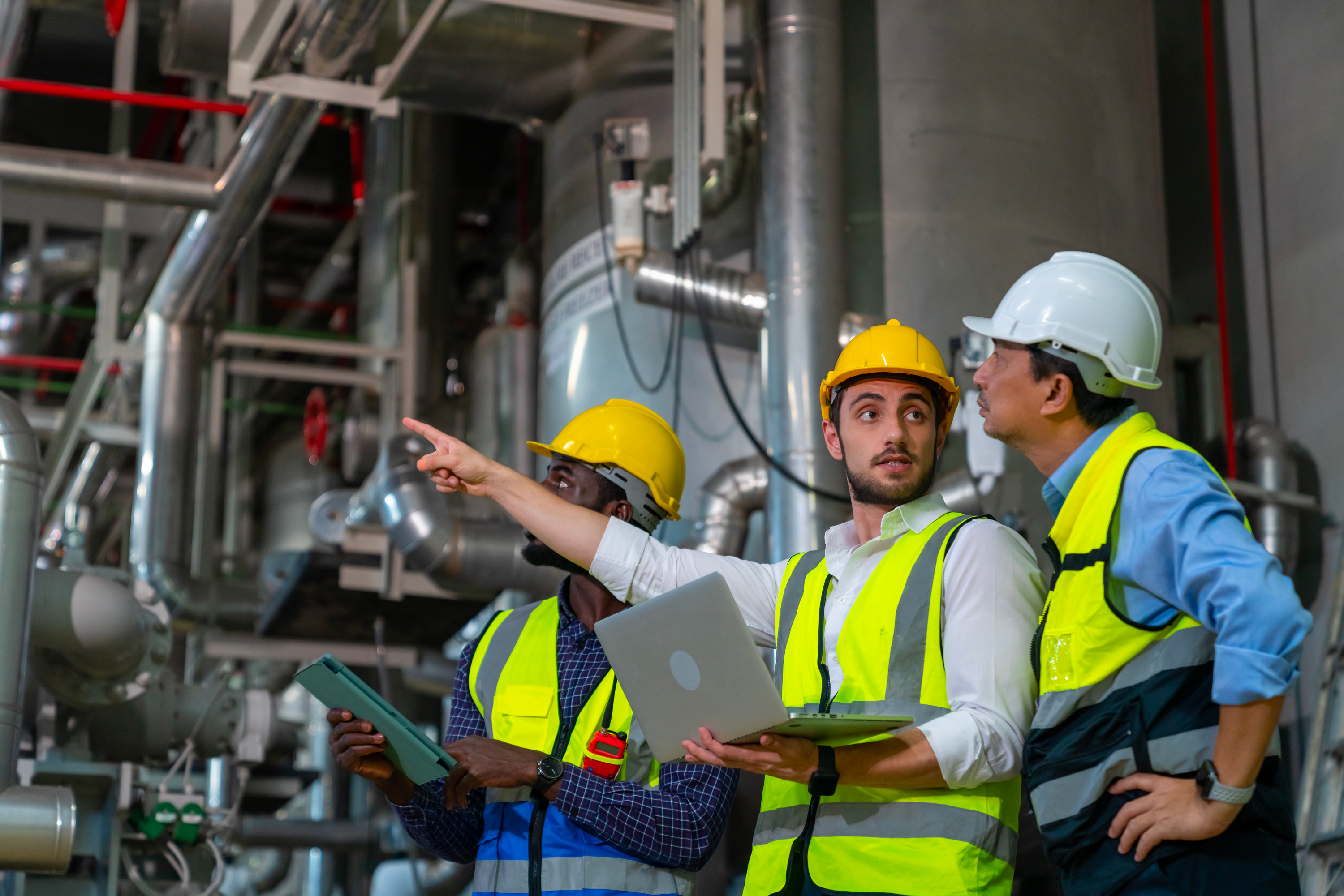 Engineers in hard hats inspecting equipment in an industrial facility, representing safety and maintenance.