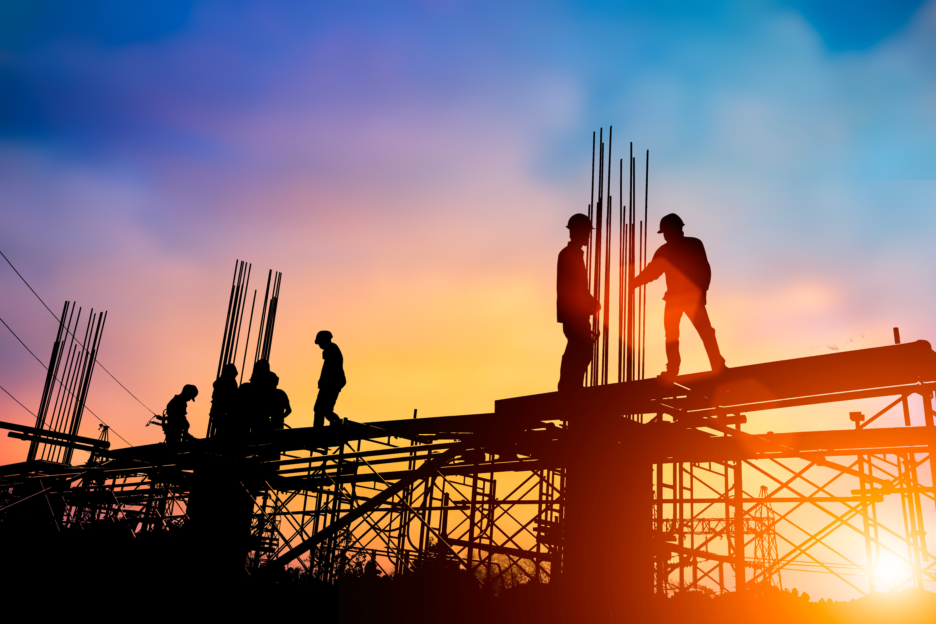 Silhouette of a worker on scaffolding at sunset, representing construction and progress.