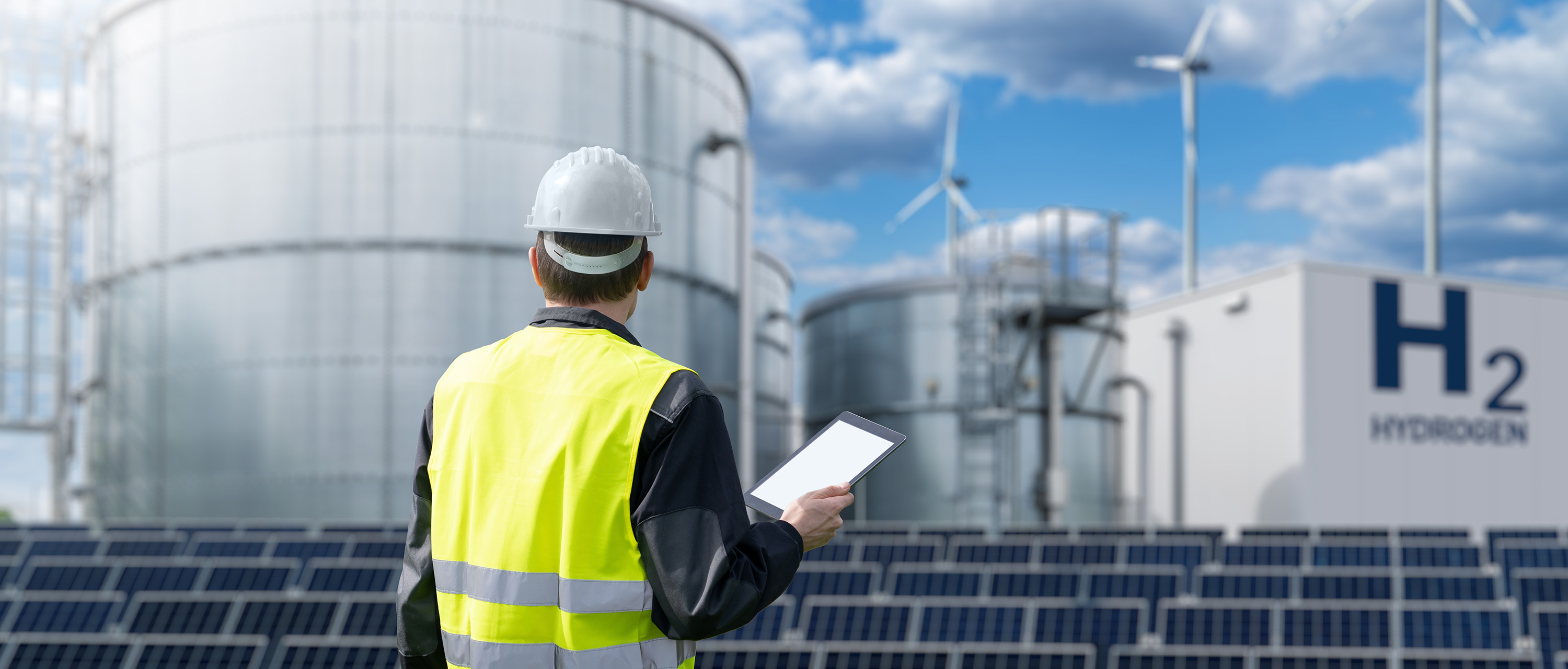 An engineer in a hard hat reviewing plans in front of industrial tanks, representing site inspection and project management.