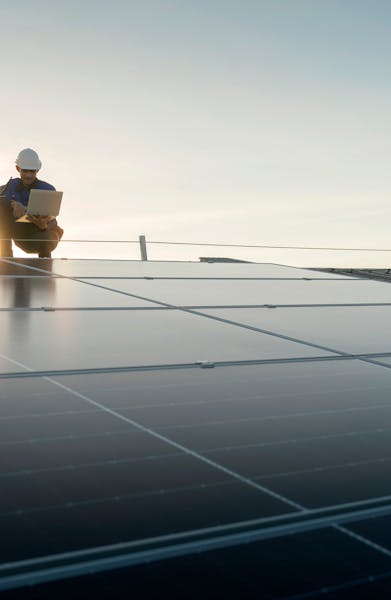 A worker walking on a solar panel installation at sunrise, representing renewable energy development.