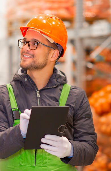 A worker wearing safety gear holding a clipboard, representing quality control and site supervision.