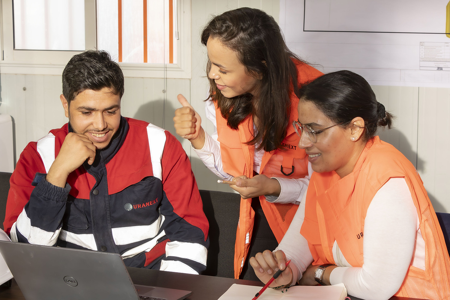 Team members collaborating around a laptop in an office, discussing a project together.