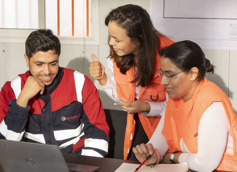 Team members collaborating around a laptop in an office, discussing a project together.