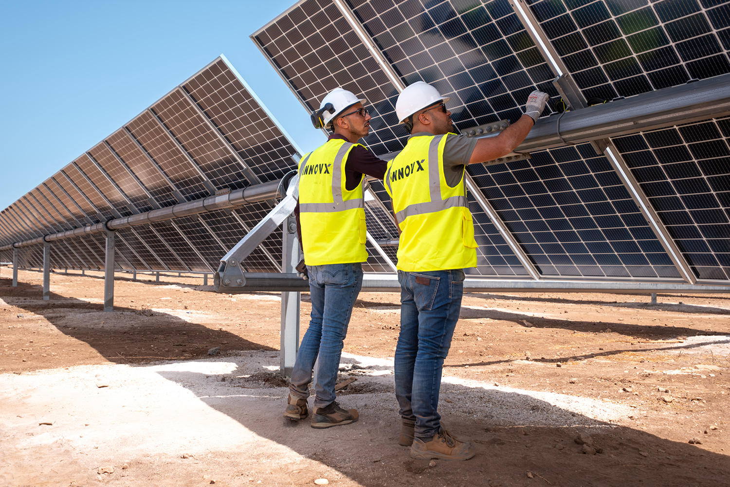 Engineers in safety vests inspecting a large solar panel installation, representing renewable energy and sustainability.