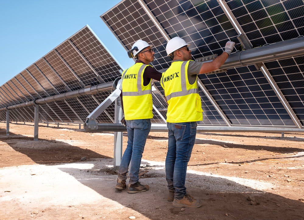 Engineers in safety vests inspecting a large solar panel installation, representing renewable energy and sustainability.