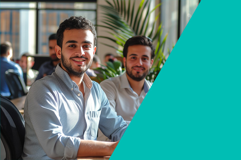 Two colleagues smiling in an office environment, suggesting teamwork and a positive workplace culture.