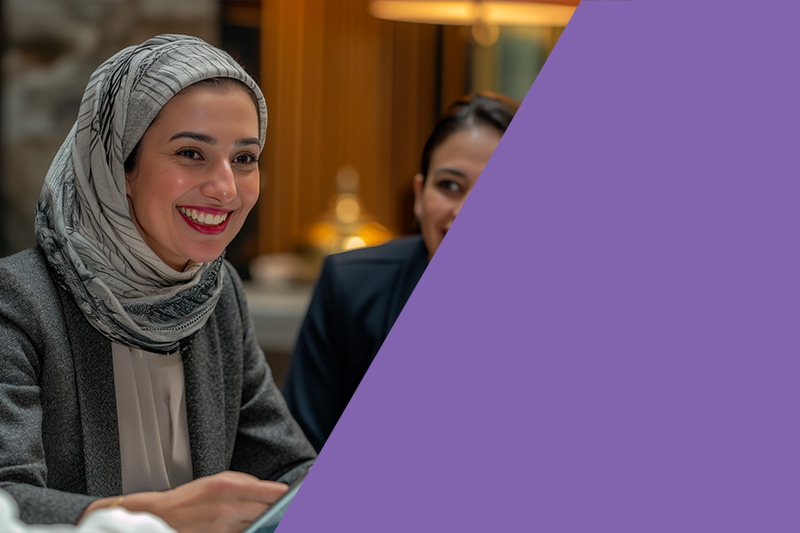 A woman wearing a headscarf smiling in a professional setting, representing inclusion and collaboration.