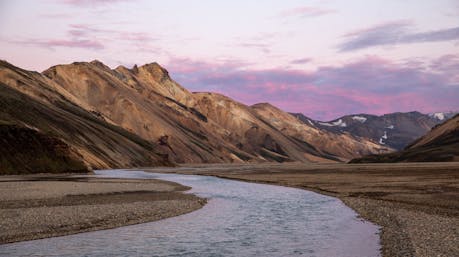 Midnight sun casting a pink glow over the mountains and river in Landmannalaugar, Iceland’s highland geothermal region.