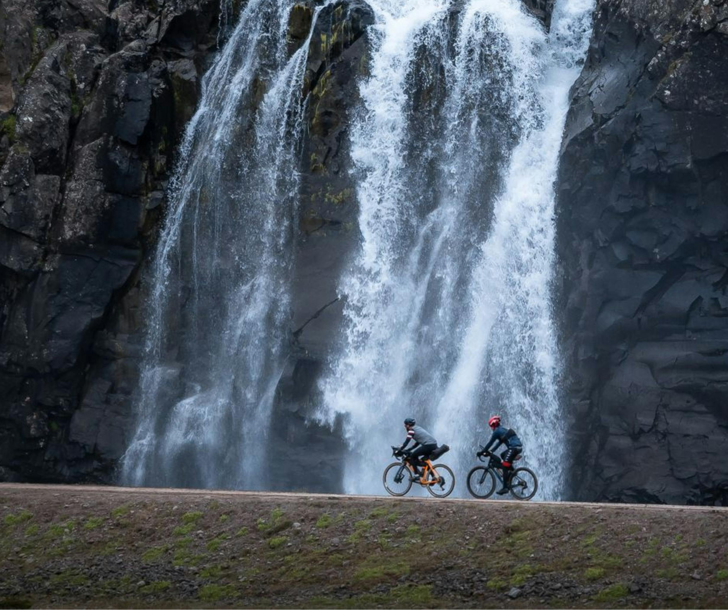 Cyclists passing by a waterfall in the Arna Westfjords Way Challenge, Cycling Westfjords.