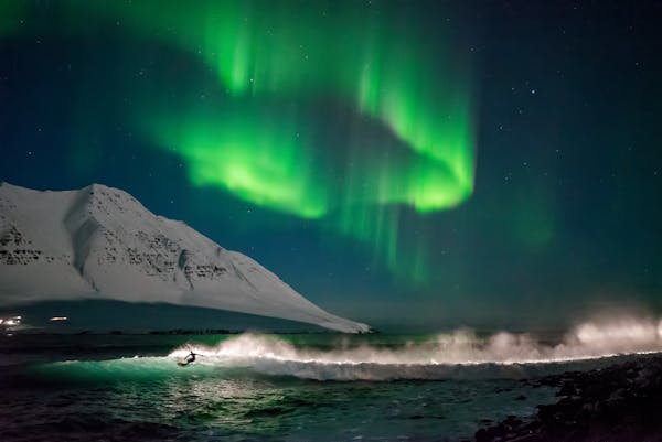A surfer on Iceland's shores with the northern lights dancing above him