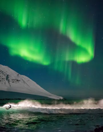 A surfer on Iceland's shores with the northern lights dancing above him