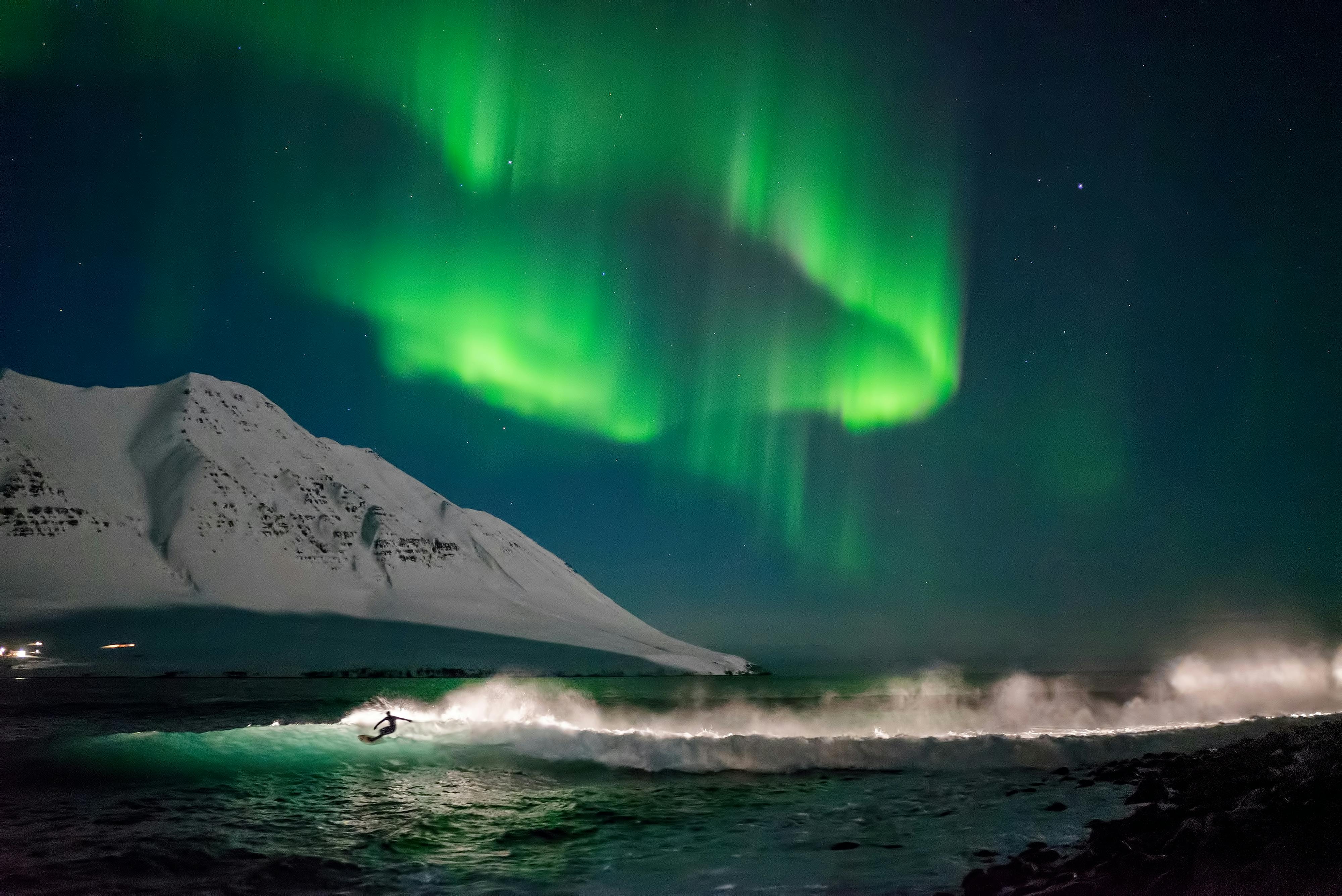 A surfer on Iceland's shores with the northern lights dancing above him