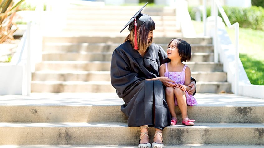 a graduate and a child holding each other and looking happy
