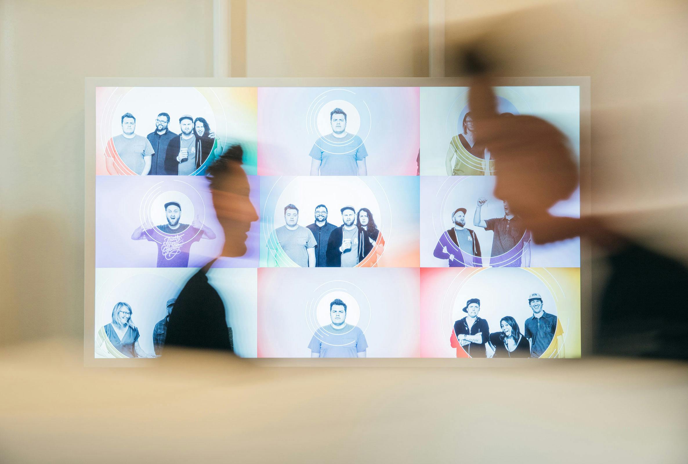 In this long exposure image, two people walk passed a TV screen that displays Emotobooth results.