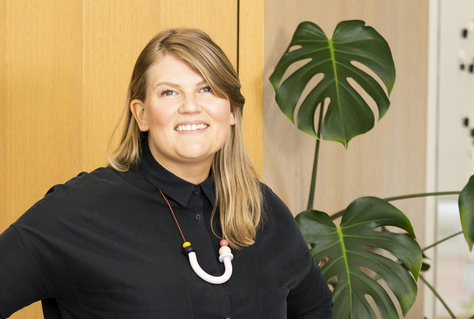 Kara Place, Instrument CEO, smiling at the camera with a thriving monstera plant behind her.