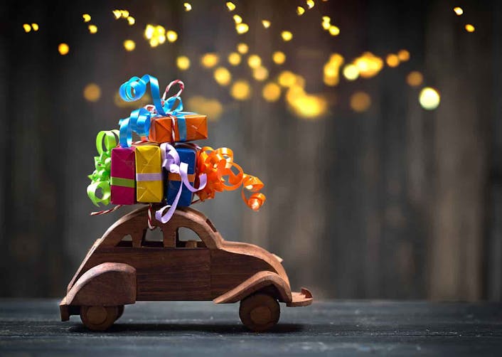 Koyu renk arka plan önünde ahşap bir oyuncak araba üzerinde renkli hediye paketleri bulunuyor.