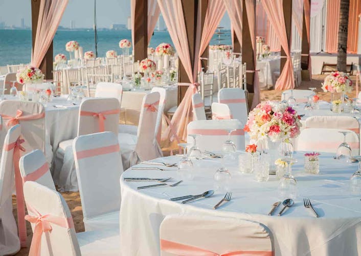 Düğün salonu içerisinde; yuvarlar masalar ve masaları çevreleyen beyaz örtüler ile kaplanmış sandalyeler duruyor. Masaların üzerinde kaşıklar, çatallar, bıçaklar ve çiçek buketleri bulunuyor.