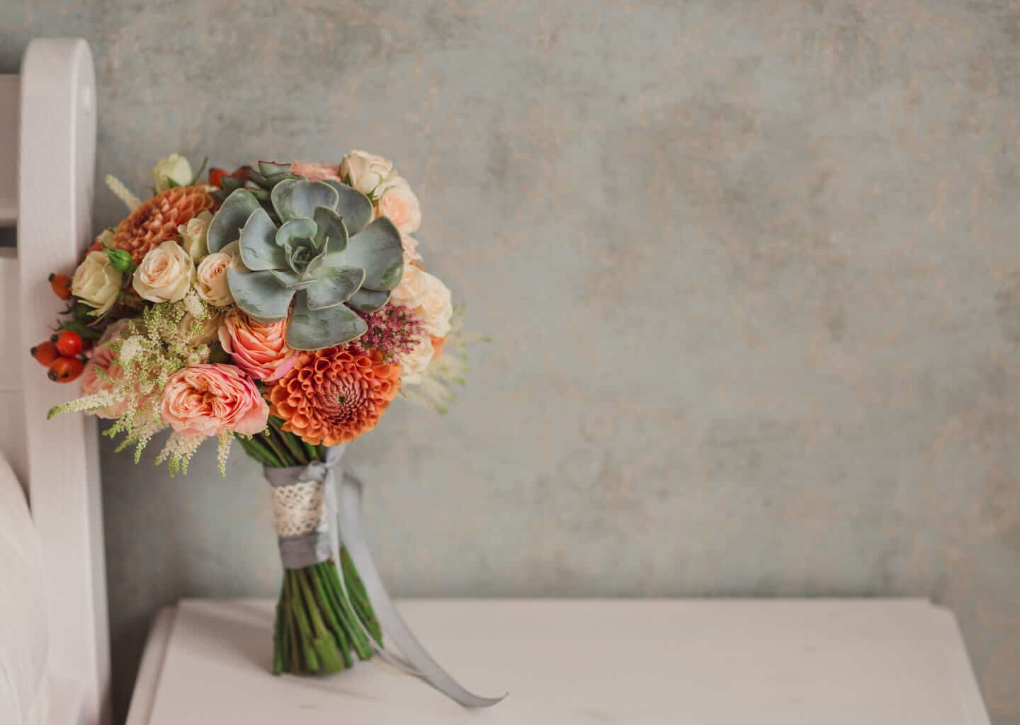 Koyu renk arka plan önünde, bir masa üzerinde sola yaslanmış şekilde bırakılan gelin çiçeği bulunuyor.