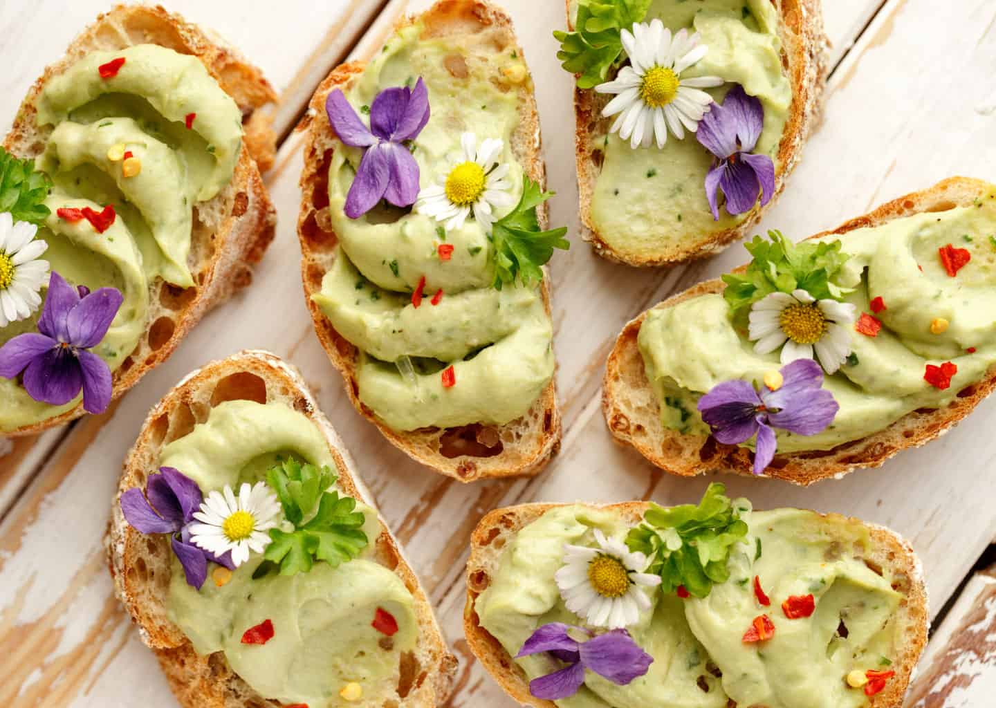 Açık renk ahşap plan üzerinde; yeşil renkli bir sos ile doldurulmuş ekmek taneleri bulunuyor.