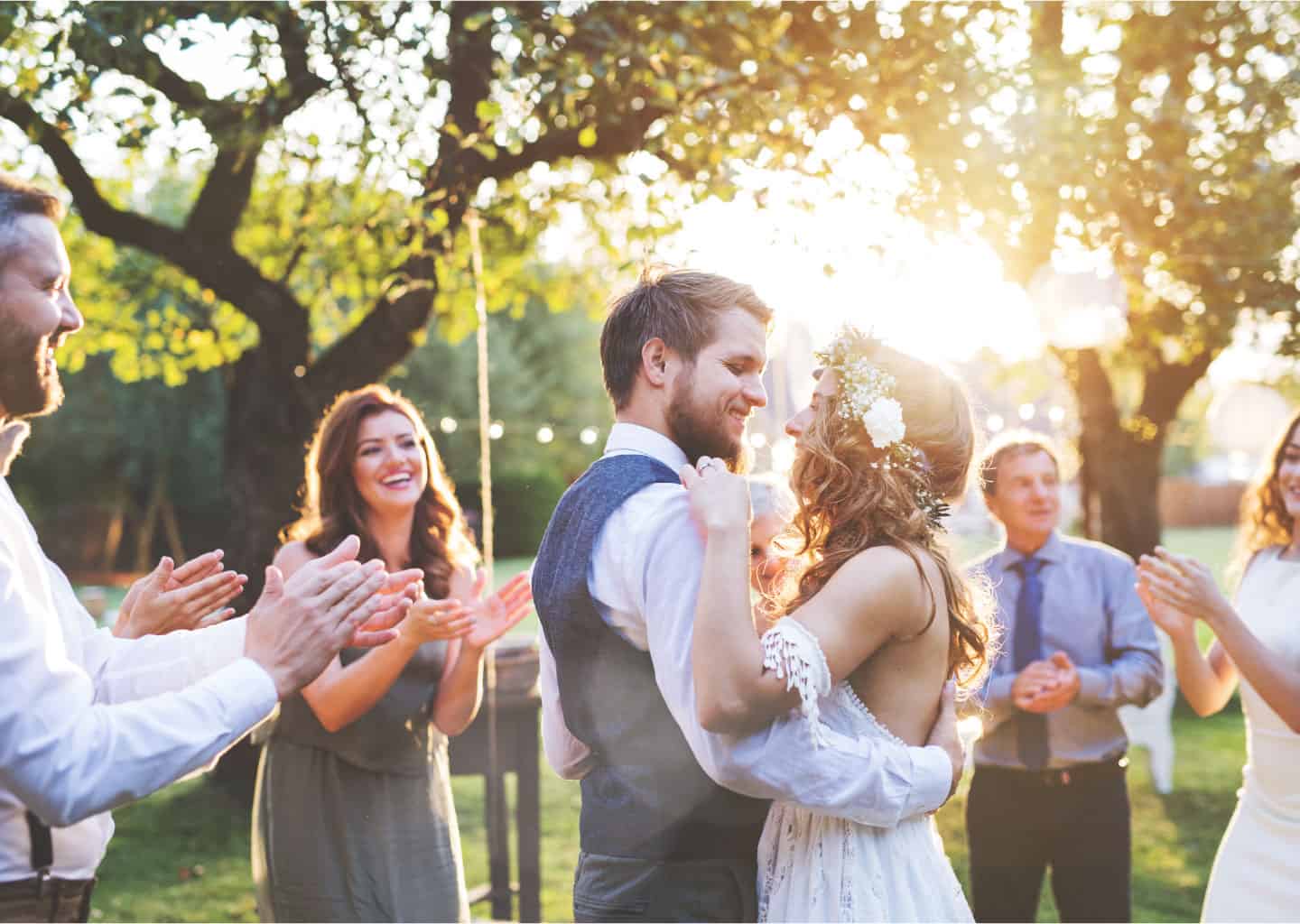 Gelin ve damat yeşillik bir bahçe içerisinde, davetlilerin ortasında dans ediyor.