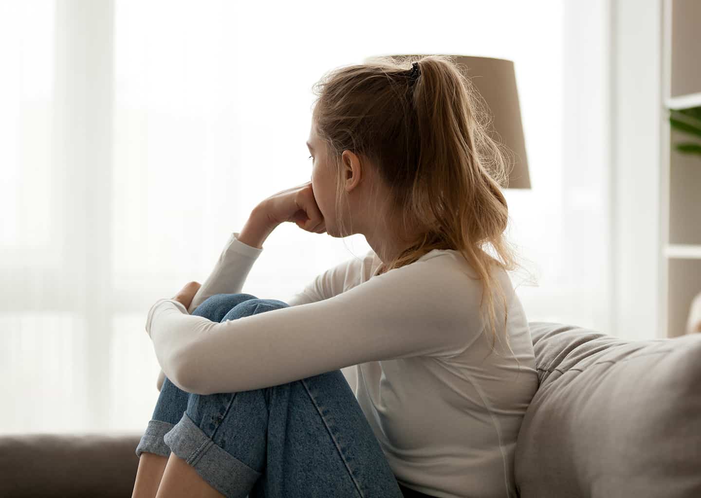 Saçlarını at kuyruğu şeklinde toplamış ve oturma odasındaki koltuk üzerinde oturan kadın, sağ eli yumruk şeklinde iken ağzını kapatarak düşüncelere dalıyor.