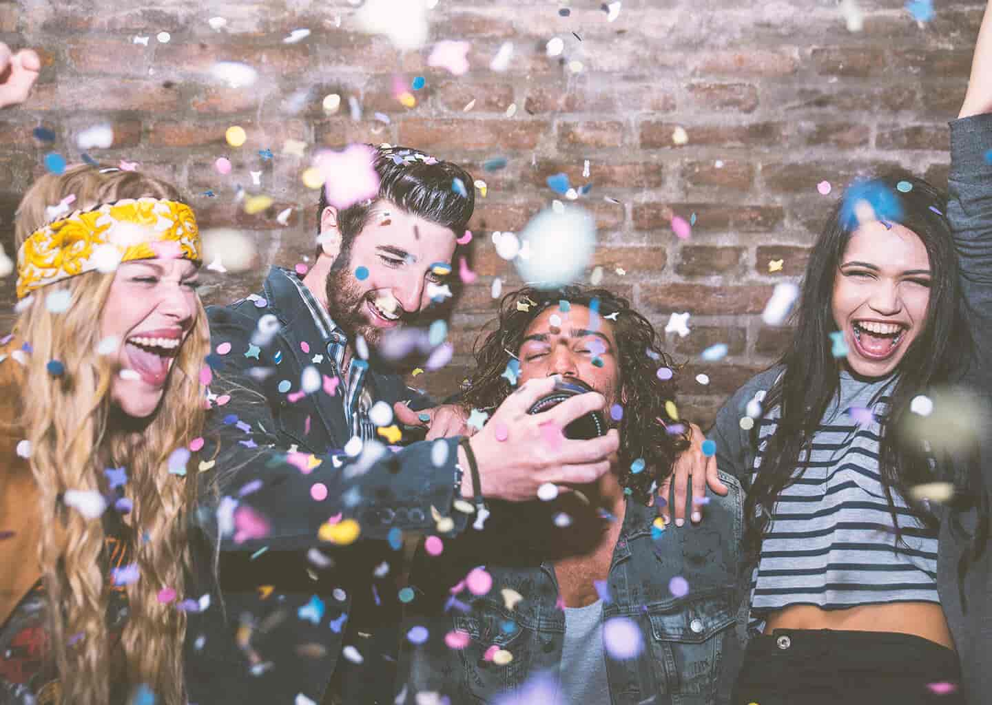 Genç arkadaş grubu gülümsüyor ve dans ediyor. Etrafta konfeti parçacıkları uçuşuyor.
