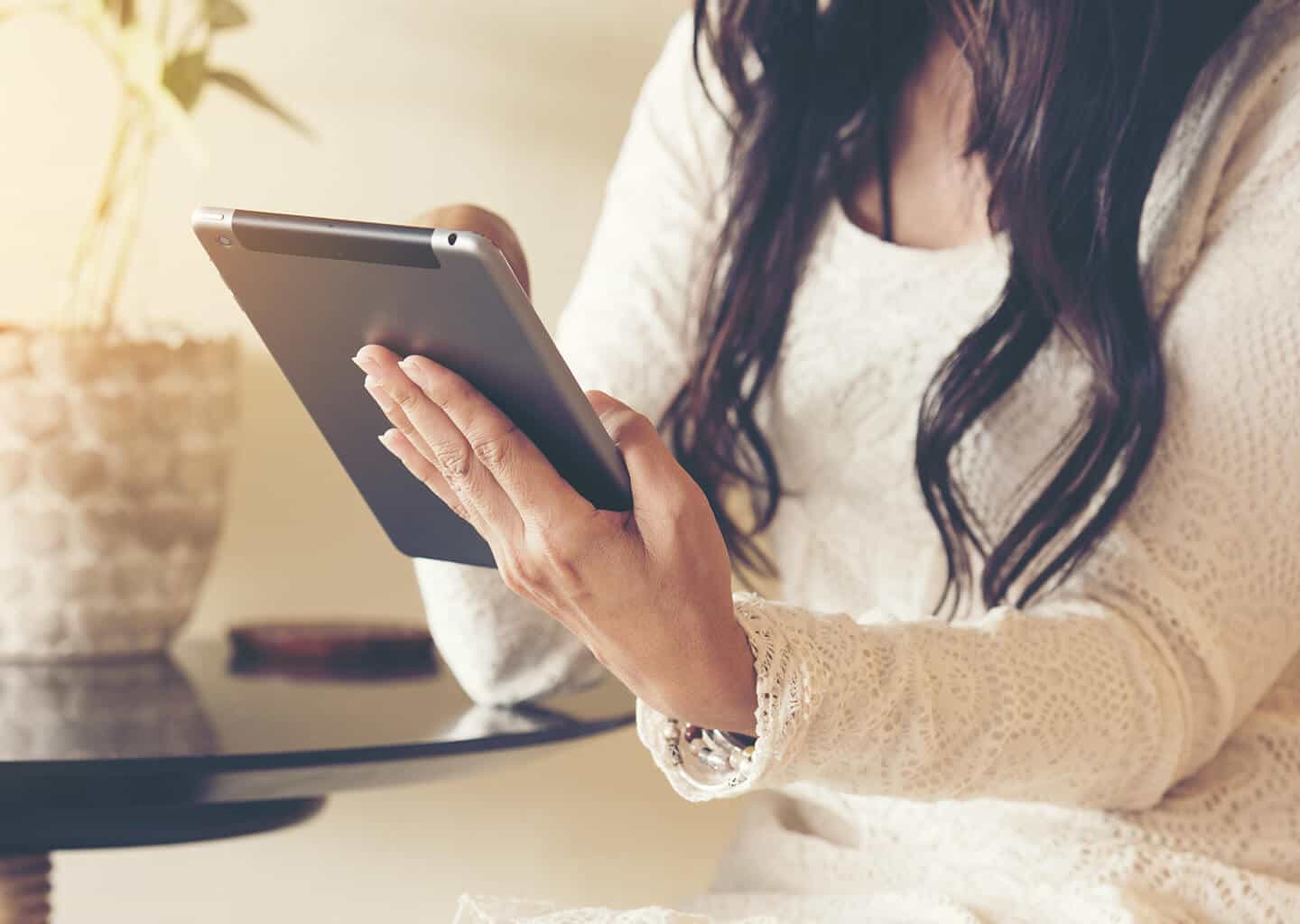 Yakın plan çekimde kadın; elinde bir tablet tutuyor. Kadının üzerinde uzun kollu ve dantel işlemeli bir gelinlik bulunuyor.