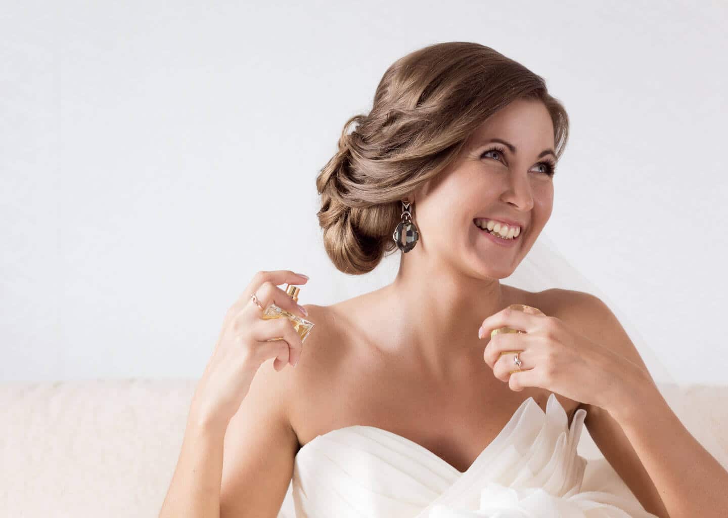 Gelin sağ ile parfümü havada tutuyor ve sola doğru bakarak gülümsüyor.