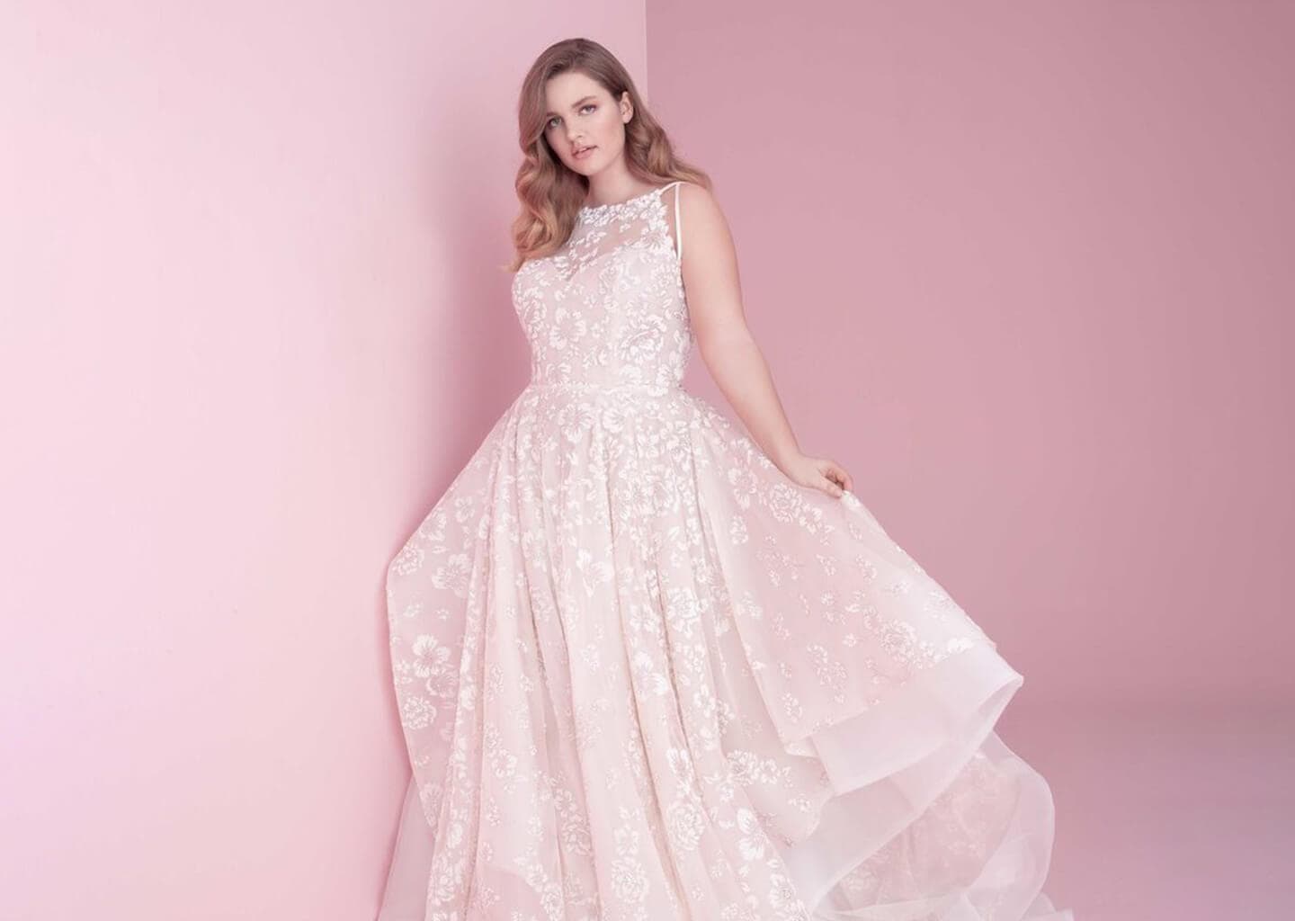 Pembe arka plan önünde duran gelin gelinliğinin eteğini havaya kaldırıyor.