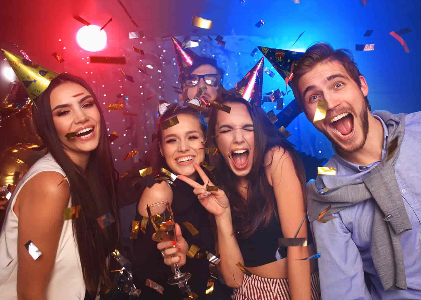 Kırmızı ve mavi ışıklandırmaların olduğu alan içerisinde genç arkadaş grubu parti şapkası takıyor ve gülümseyerek poz veriyor. 