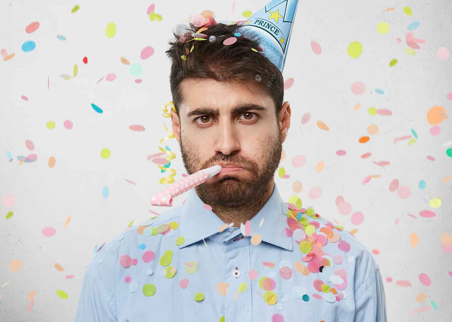 Kafasında parti şapkası olan, etrafında ve gömleğinin üzerinde konfeti parçaları bulunan genç adam somurtuyor. Genç adamın ağzında parti düdüğü bulunuyor.