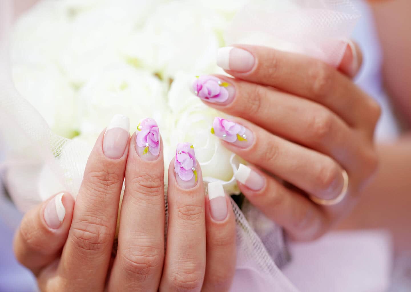 Yakın plan çekimde gelin; tırnaklarına mor renkler ile çizilmiş olan çiçek desenlerini gösteriyor.